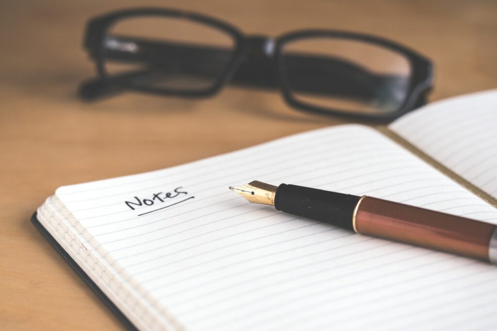 An open notebook with a fountain pen and reading glasses