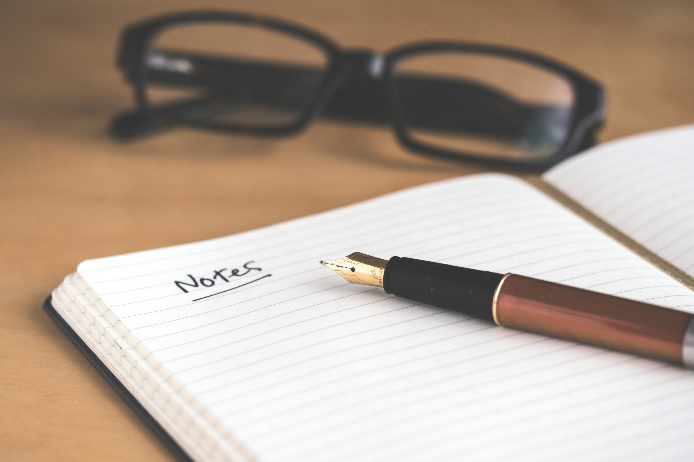 An open notebook with a fountain pen and reading glasses